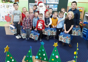 Dzieci pozują do zdjęcia wraz z Mikołajem i swoimi prezentami.