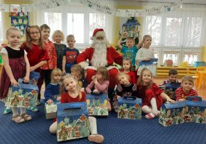 Wspólne zdjęcie dzieci wraz z Mikołajem i prezentami.