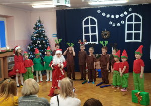 Występ dzieci przed rodzicami z okazji świąt Bożego Narodzenia. Na sali dzieci przebrane za renifery, elfy oraz Mikołaja śpiewają piosenki, recytują wiersze, grają na instrumentach, tańczą.