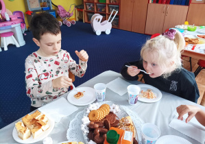 dziewczynka i chłopiec przy stoliku zjadają różne potrawy