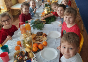 Dzieci siedzą przy stole na którym są smakołyki przyniesione przez rodziców.