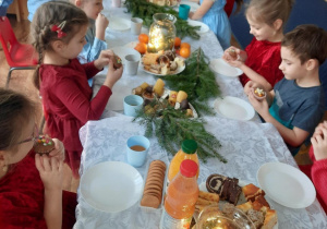 Dzieci siedzą przy stole i zjadają smakołyki przyniesione przez rodziców.