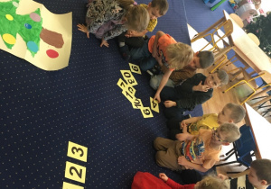 Dzieci siedzą na dywanie i układają cyfry.