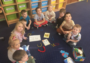 Dzieci siedzą w kole na dywanie przed nimi ilustracje i ukształtowane z drucików literki "u".