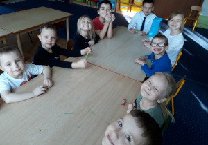 Dzieci siedzą przy stole i trzymają cukierki w dłoni.