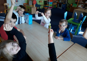 Dzieci siedzą przy stole i trzymają cukierki w dłoni.