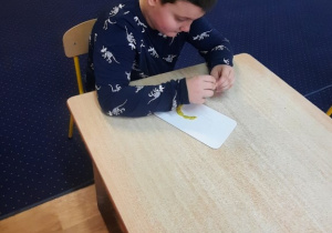 Chłopiec siedzi przy stole i wykleja cyfrę 5.