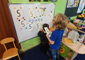 Dzieci mocują na tablicy cyfrę 5.