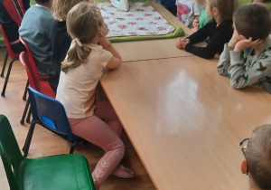 Dzieci zgromadzone wokół stołu, a chłopiec prasuje wraz z panią.