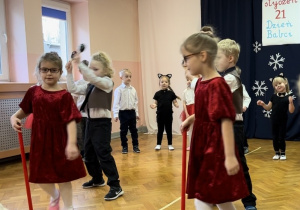 Dzieci ustawione w półkolu śpiewają piosenkę, czworo tańczy na środku sali.