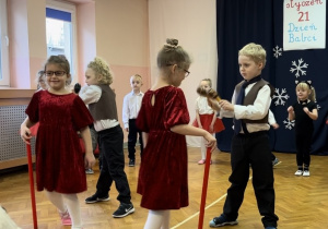 Dzieci ustawione w półkolu śpiewają piosenkę, czworo tańczy na środku sali.