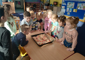 dzieci stoją dookoła stolików, na których widać upieczone trójkątne kawałki pizzy