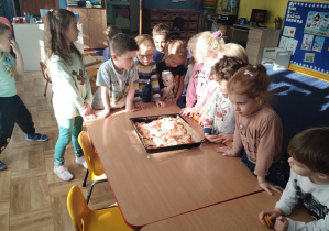 dzieci stoją dookoła stolików, na których widać upieczone trójkątne kawałki pizzy