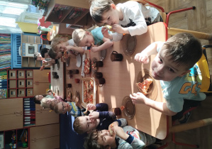 dzieci siedzą przy stolikach, na których widać upieczone trójkątne kawałki pizzy, jedzą pizzę
