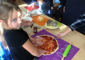 Dzieci układają szynkę na pizzy.