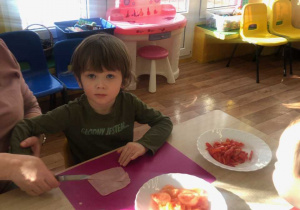 Chłopiec siedzi przy stole i kroi szynkę.
