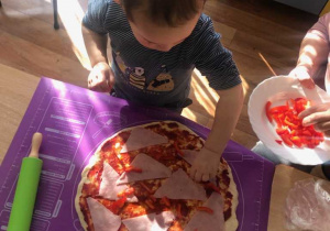 Chłopiec układa szynkę na pizzy.