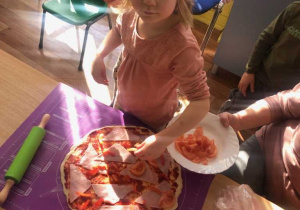 Dziewczynka układa pomidory na pizzy.