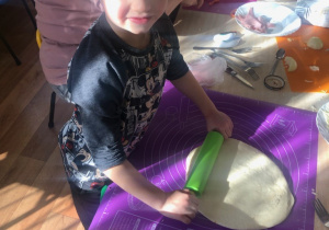 Chłopiec wałkuje ciasto na pizzę.