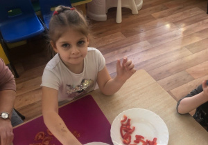 Dziewczynka siedzi przy stole i układa pokrojone pomidory na talerzu.