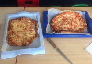 Na stole leżą dwie pizze wykonane przez dzieci i gotowe do upieczenia.
