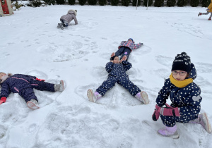 Dzieci leżą na śniegu i robią "orzełki".