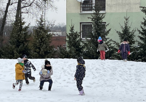 Dzieci biegają , a dziewczynka podnosi kulę ze śniegu.