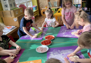 Dzieci przy stole wałkują ciasto i formują kształt koła z ciasta.