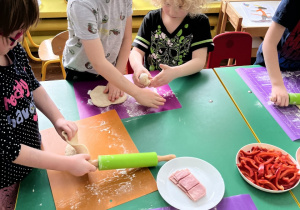 Dzieci przy stole wałkują ciasto i formują kształt koła z ciasta.