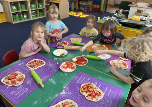 Dzieci przy stołach przygotowują pizzę dla siebie, nakładają składniki.