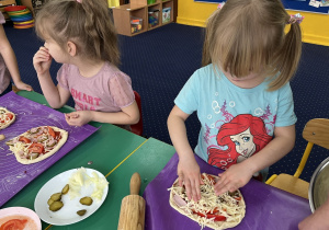Dzieci przy stołach przygotowują pizzę dla siebie, nakładają składniki.