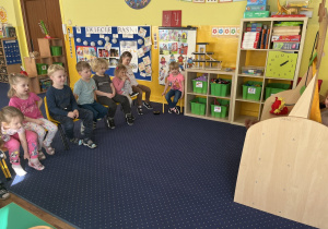Dzieci na krzesłach obserwują przedstawienie w wykonaniu kolegów,