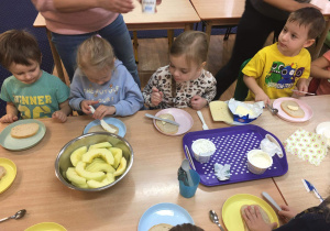 Dzieci siedzą przy stole i przygotowują sobie jedzenie z produktów mlecznych.