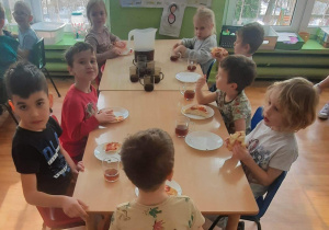 Dzieci siedzą przy stole i zjadają pizzę.