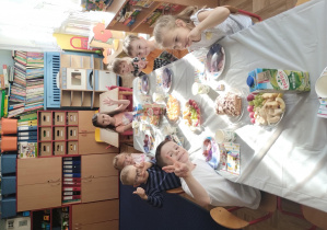 dzieci siedzą przy stolikach, na których ustawione są talerzyki ze smakołykami