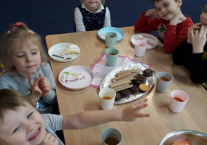 Dzieci siedza przy stole na którym stoją słodkości.