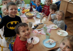 Dzieci siedza przy stole na którym stoją słodkości.