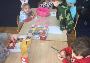 Dzieci siedzą przy stoliku i bawią się prezentując różne zawody.