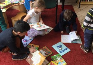 Dzieci siedzą w bibliotece na dywanie i oglądają książki