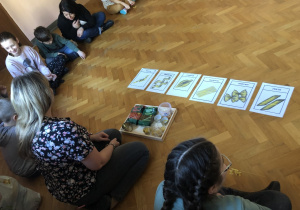 Dzieci siedzą na podłodze w kole, a przed nimi leżą ilustracje różnych makaronów.