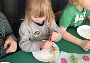 Dzieci siedzą przy stole i nawijają spaghetti na widelec.