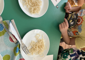Dzieci siedzą przy stole odwzorowują kształty z wykorzystaniem makaronu.