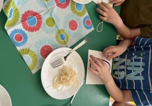 Dzieci siedzą przy stole odwzorowują kształty z wykorzystaniem makaronu.