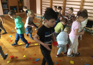 Dzieci przemieszczają się po sali gimnastycznej wśród figur geometrycznych.