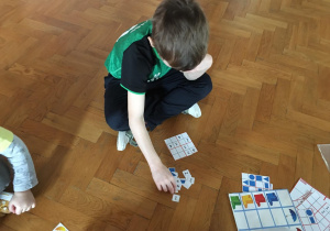 Chłopiec siedzi na podłodze i wyszukuje odpowiedniej cyfry.