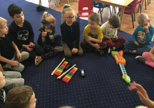 Dzieci siedzą na dywanie w kole i oglądają instrumenty.