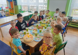 Dzieci siedzą przy stole na którym stoją słodkości.