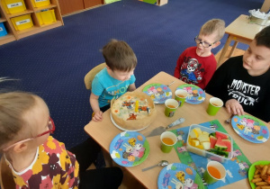 Dzieci siedzą przy stole na którym stoją słodkości.