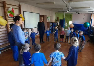 grupa dzieci ubrana na niebiesko tańczy w dużym kole na sali gimnastycznej