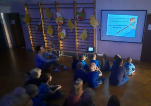 grupa dzieci ubrana na niebiesko ogląda film na dużym ekranie na sali gimnastycznej